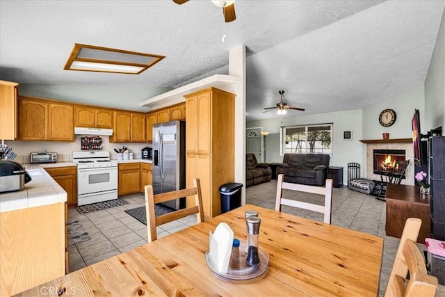 kitchen featuring lofted ceiling, a ceiling fan, white range with gas stovetop, and stainless steel fridge