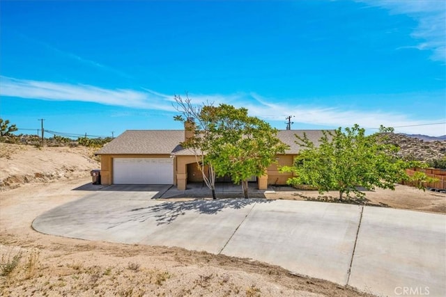 view of property hidden behind natural elements featuring stucco siding, driveway, and an attached garage