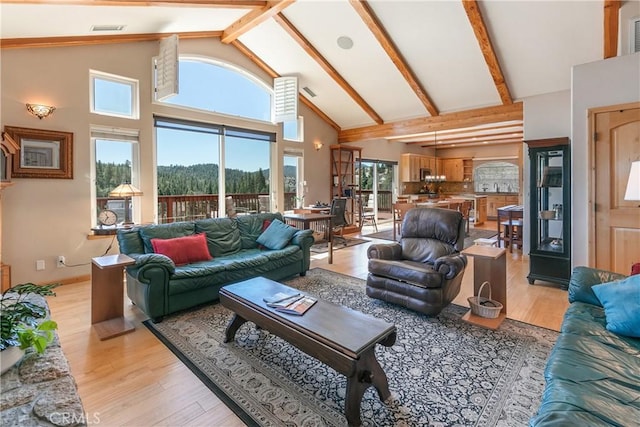 living area featuring light wood finished floors, visible vents, high vaulted ceiling, and beamed ceiling