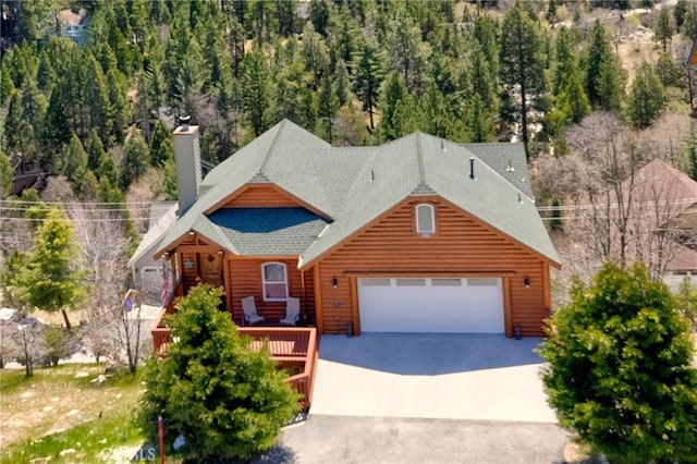 view of front of property featuring a chimney, faux log siding, roof with shingles, concrete driveway, and an attached garage