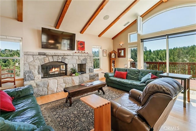 living room featuring wood finished floors, beamed ceiling, a stone fireplace, visible vents, and high vaulted ceiling