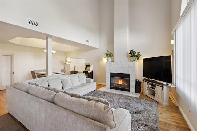 23684 Valley View Rd, Calabasas, CA 91302 - living room with light wood-style flooring, a fireplace, baseboards, visible vents, and a towering ceiling