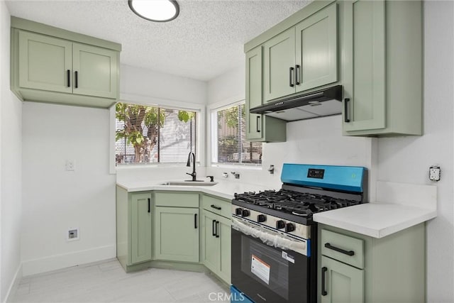 kitchen with a sink, under cabinet range hood, green cabinets, light countertops, and stainless steel gas range oven