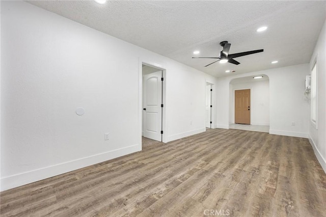 spare room with recessed lighting, a ceiling fan, baseboards, arched walkways, and wood finished floors