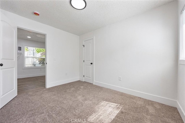 carpeted spare room featuring a textured ceiling and baseboards