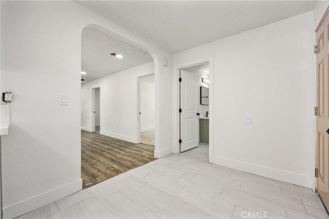 spare room with a textured ceiling, light wood-style floors, baseboards, and arched walkways