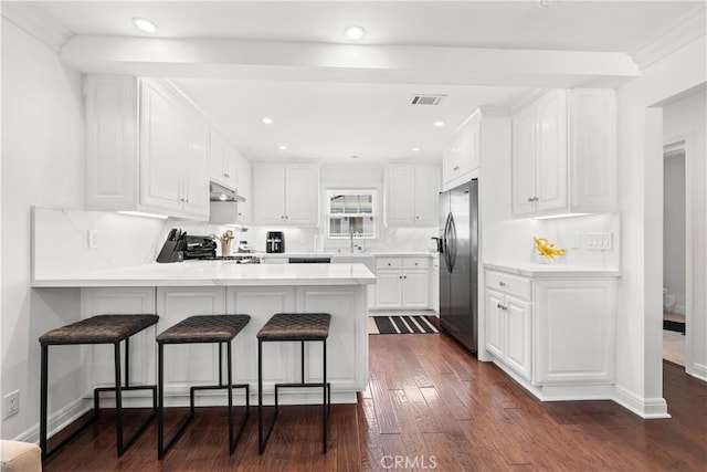 kitchen with range, under cabinet range hood, dark wood-style flooring, a peninsula, and stainless steel fridge with ice dispenser