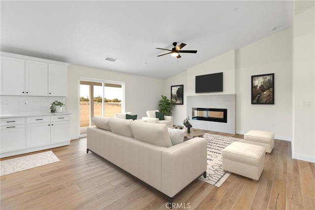 living area featuring vaulted ceiling, a fireplace, light wood finished floors, visible vents, and a ceiling fan