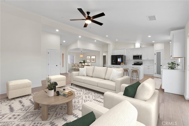 living room featuring visible vents, vaulted ceiling, light wood-style floors, and recessed lighting