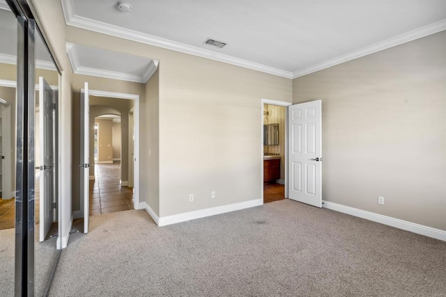 unfurnished bedroom with carpet floors, arched walkways, baseboards, and visible vents