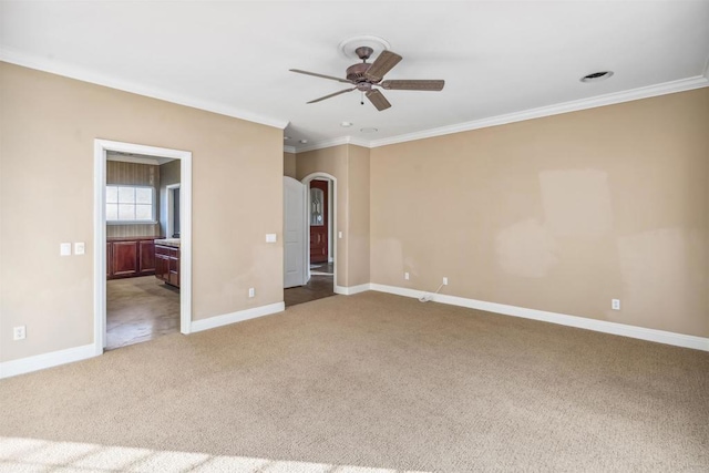 unfurnished bedroom featuring crown molding, carpet flooring, baseboards, ensuite bathroom, and arched walkways