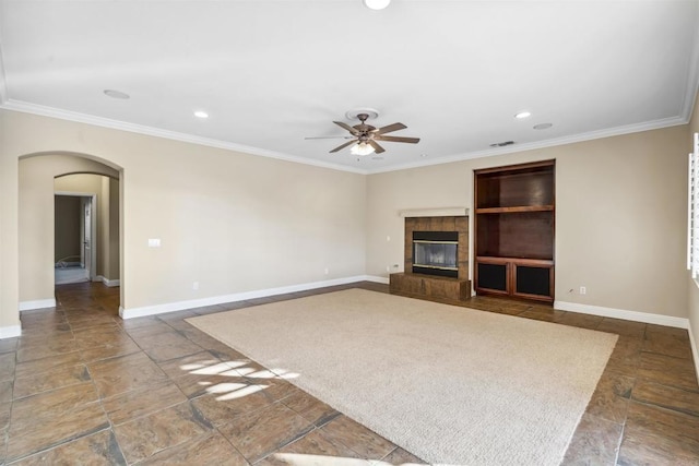 unfurnished living room with crown molding, arched walkways, a ceiling fan, and baseboards