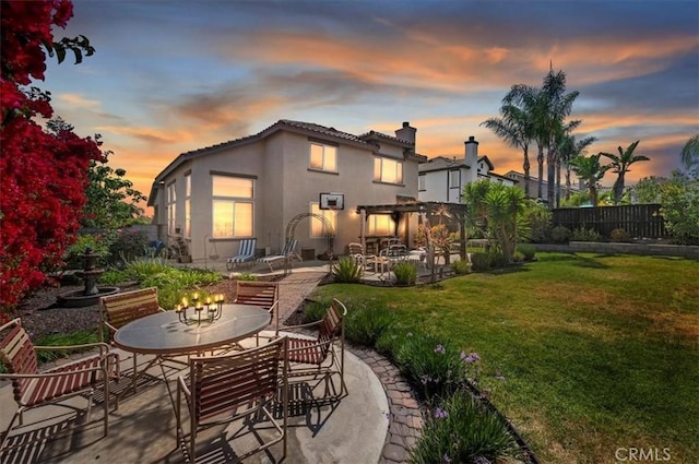 back of property at dusk with a fenced backyard, outdoor dining space, a patio area, and stucco siding