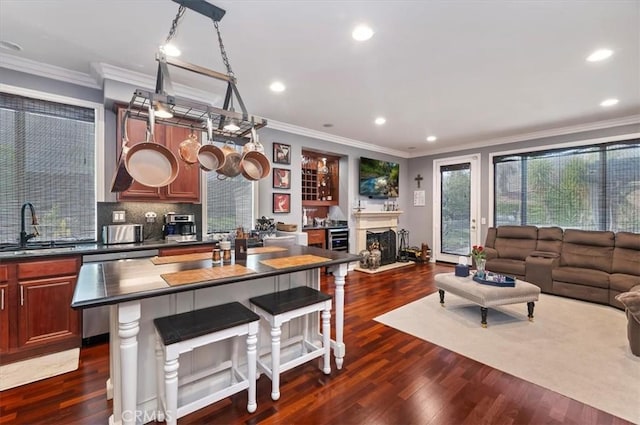 kitchen with dark countertops, stainless steel dishwasher, a sink, dark wood-style floors, and open floor plan