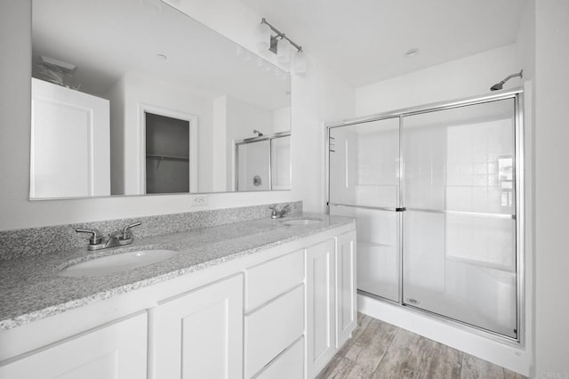 bathroom featuring a stall shower, wood finished floors, double vanity, and a sink