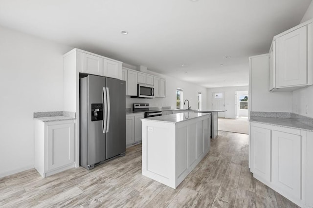 kitchen featuring stainless steel appliances, a center island, a sink, light wood-type flooring, and a peninsula