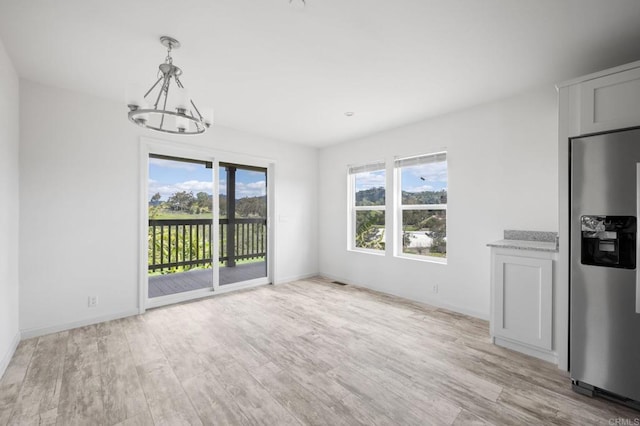 unfurnished dining area with an inviting chandelier, baseboards, and light wood-style floors