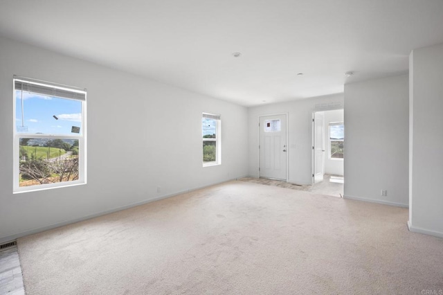 unfurnished room with a wealth of natural light, light carpet, and baseboards