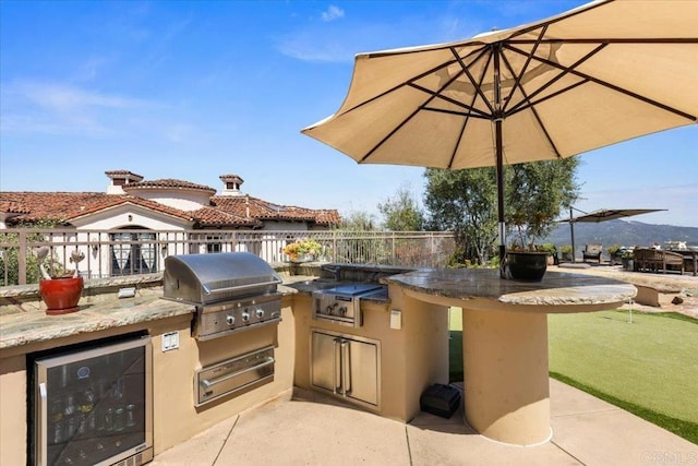 view of patio / terrace with beverage cooler, fence, area for grilling, and an outdoor kitchen
