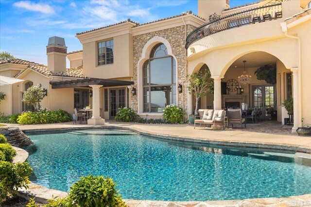 back of property with french doors, an outdoor pool, a balcony, a patio, and stucco siding