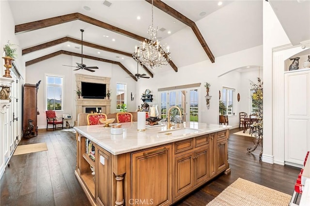 kitchen featuring a sink, brown cabinetry, arched walkways, open floor plan, and ceiling fan with notable chandelier