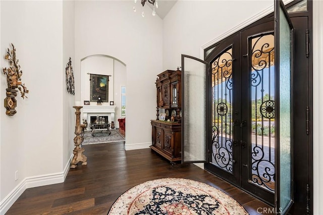entryway with a high ceiling, baseboards, arched walkways, french doors, and wood finished floors