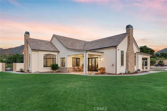 back of property at dusk featuring a lawn, stucco siding, and a chimney
