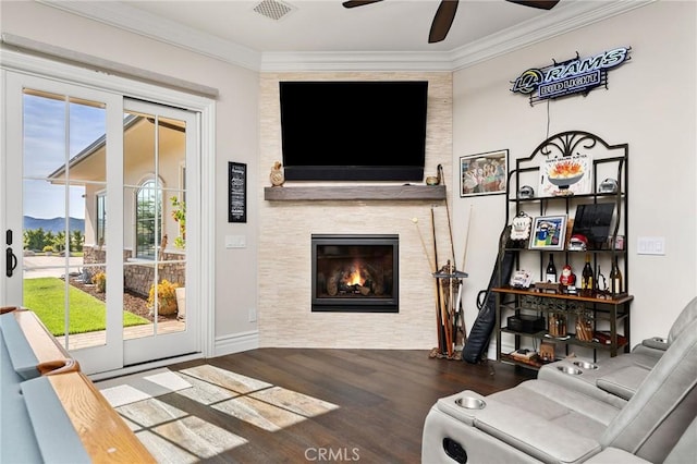 living room with a tile fireplace, ceiling fan, crown molding, visible vents, and wood finished floors
