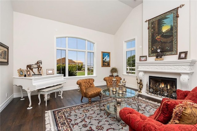 sitting room with a warm lit fireplace, high vaulted ceiling, wood finished floors, and baseboards