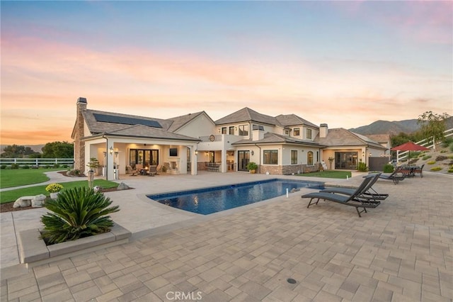 pool at dusk featuring outdoor dining area, a patio area, ceiling fan, an outdoor pool, and fence