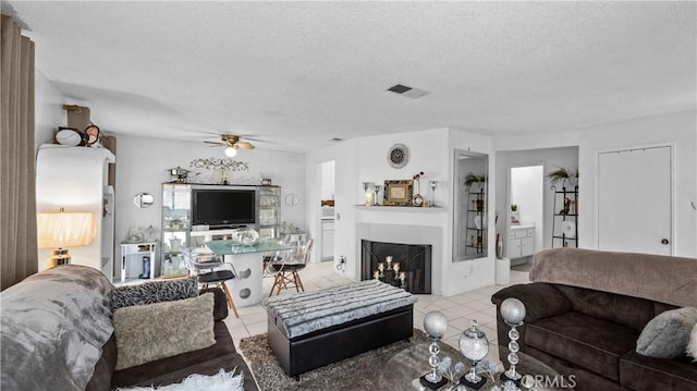 living room featuring light tile patterned floors, a ceiling fan, visible vents, and a textured ceiling