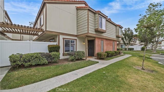 townhome / multi-family property featuring brick siding, fence, a front yard, and a pergola