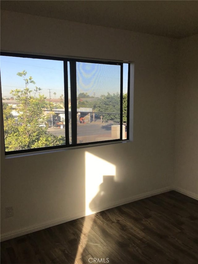 empty room featuring dark wood finished floors, baseboards, and a healthy amount of sunlight
