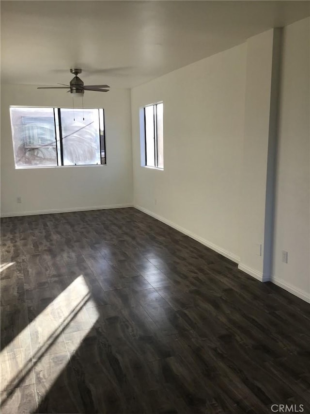 empty room with baseboards, a ceiling fan, and dark wood-type flooring