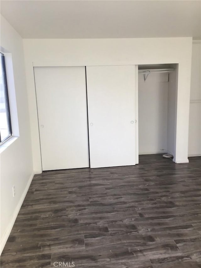 unfurnished bedroom with dark wood finished floors, baseboards, and a closet