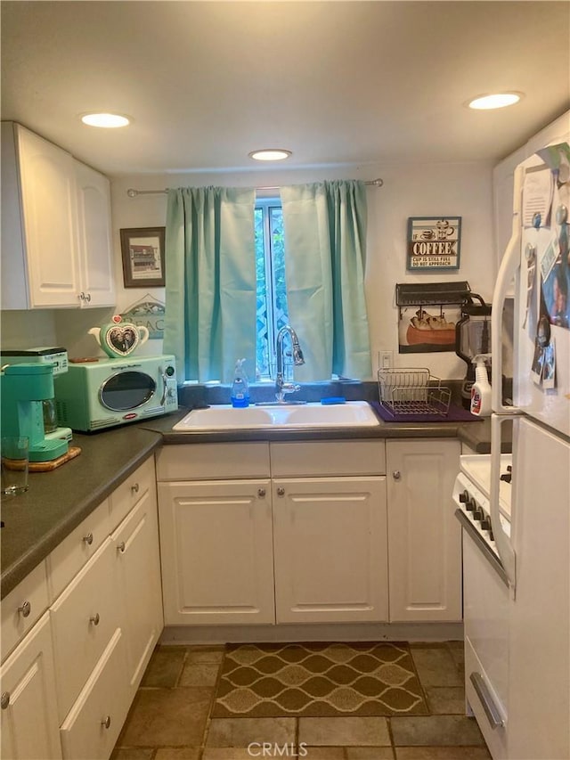 kitchen featuring white appliances, white cabinets, dark countertops, and a sink