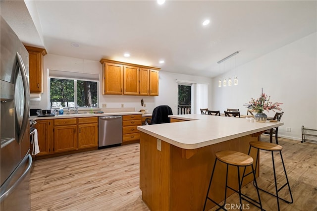kitchen featuring brown cabinetry, stainless steel appliances, a kitchen breakfast bar, and light countertops