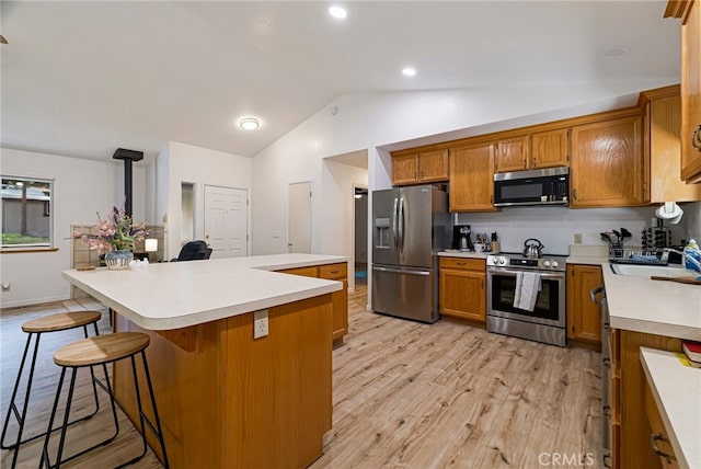 kitchen with a sink, vaulted ceiling, brown cabinets, and appliances with stainless steel finishes