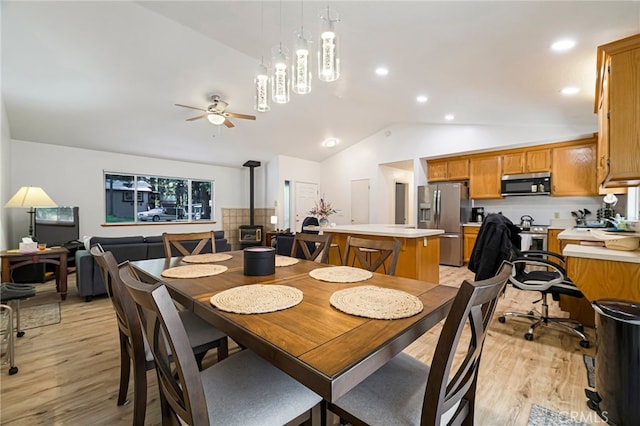 dining area featuring a wood stove, light wood finished floors, ceiling fan, and lofted ceiling