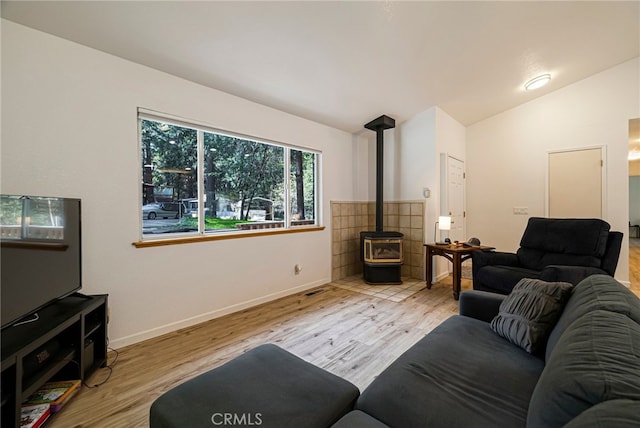 living area with a wood stove, wood finished floors, lofted ceiling, and baseboards