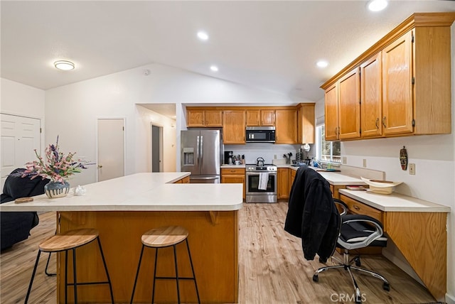 kitchen featuring stainless steel appliances, brown cabinets, a kitchen bar, light wood finished floors, and lofted ceiling