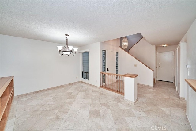 empty room featuring a textured ceiling, a chandelier, and baseboards