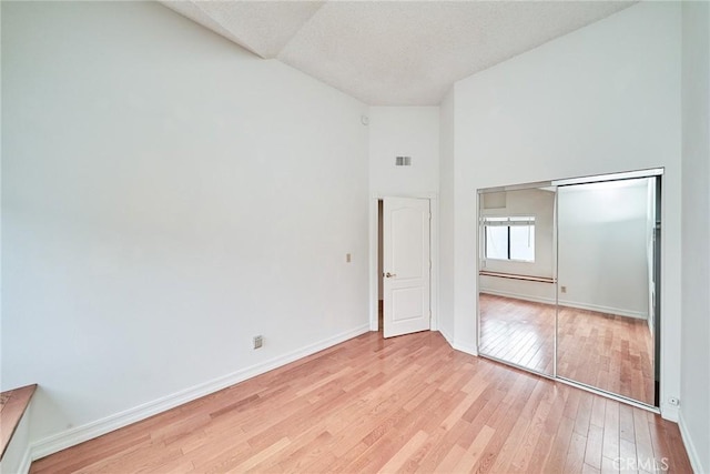 spare room with high vaulted ceiling, baseboards, light wood-style flooring, and visible vents