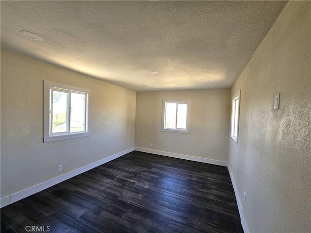 spare room featuring a textured ceiling, a textured wall, dark wood finished floors, and baseboards