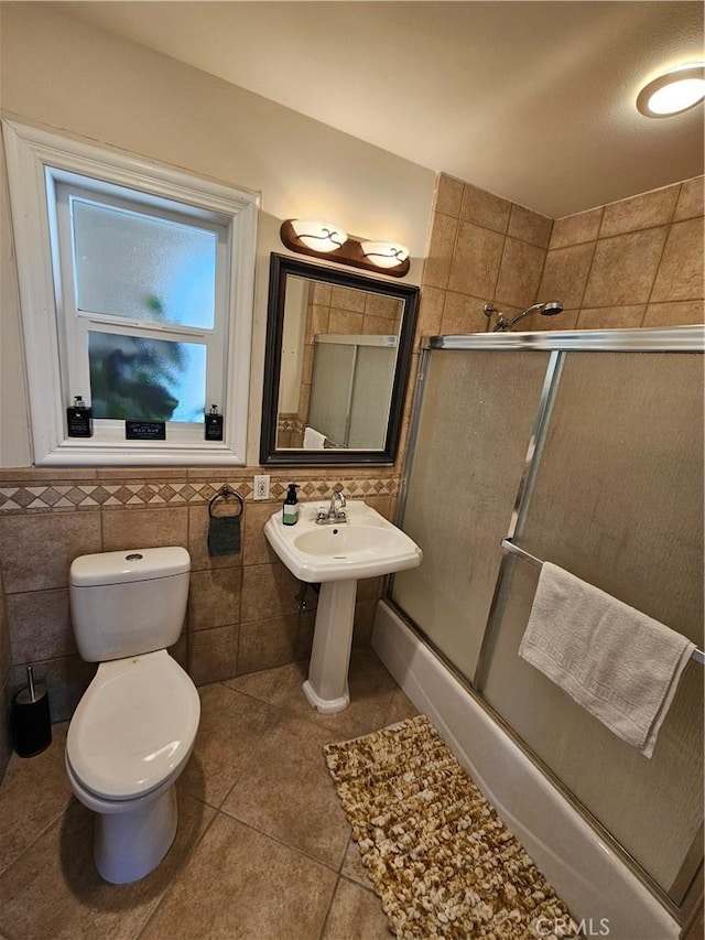 bathroom with tile walls, a sink, toilet, a wainscoted wall, and tile patterned flooring