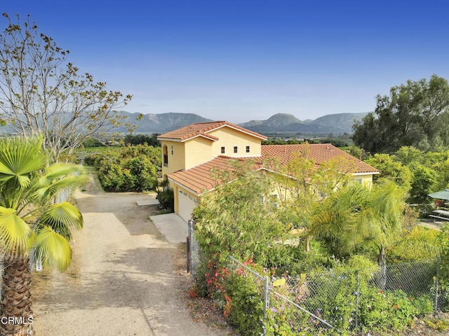 view of property exterior featuring stucco siding, a tiled roof, dirt driveway, a mountain view, and an attached garage