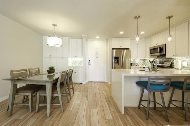 999 N Pacific St Unit E108, Oceanside, CA 92054 - kitchen featuring white cabinetry, light wood-style flooring, appliances with stainless steel finishes, a peninsula, and backsplash