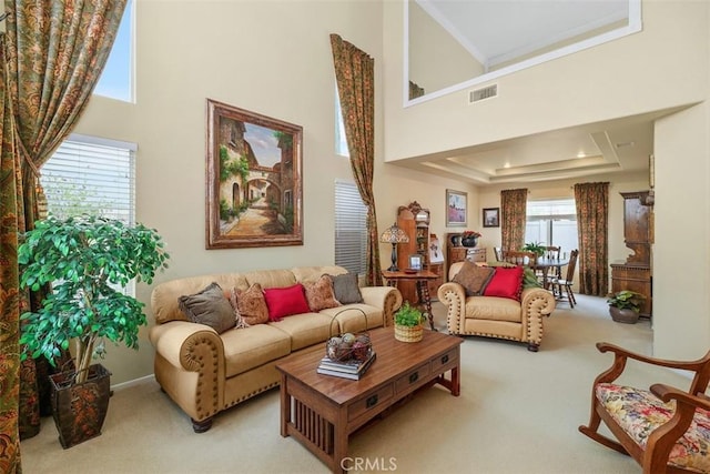 carpeted living area with crown molding, a high ceiling, visible vents, and a raised ceiling
