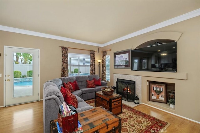 living room featuring a tile fireplace, wood finished floors, ornamental molding, and baseboards