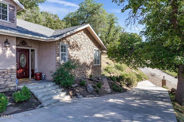 view of exterior entry with stone siding, stucco siding, and roof with shingles